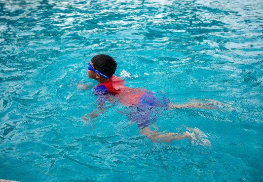 boy wearing a swimsuit and glasses swimming in the middle of the pool with a blue water background