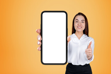 Fototapeta na wymiar Businesswoman with thumb up, phone empty display on yellow background