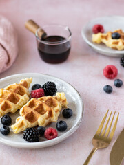 Croffles (combination of croissant and waffle) with fresh raspberry, blueberry and blackberry served in ceramic plate on pink table. Kitchen towel on background. Food trend from South Asia. Close up