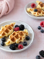 Croffles (combination of croissant and waffle) with fresh raspberry, blueberry and blackberry served in ceramic plate on pink table. Kitchen towel on background. Food trend from South Asia. Close up