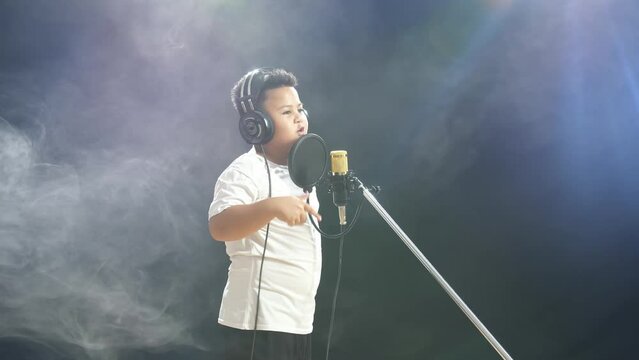 Young Asian Boy With Headphone Rapping Into A Condenser Microphone On The White Smoke Black Background
