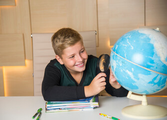 surprised schoolboy with a magnifying glass researching a globe in the classroom