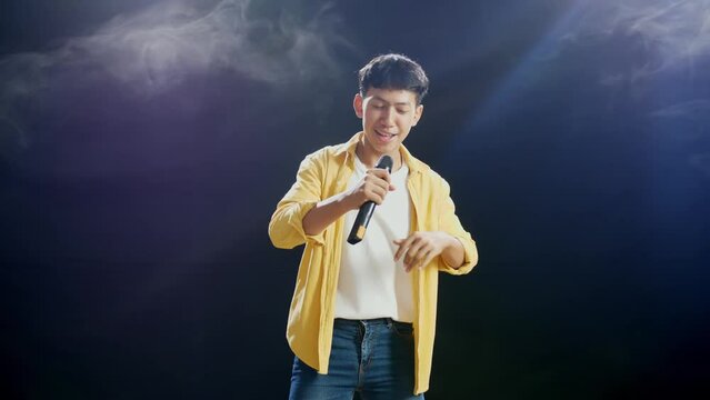 Young Asian Boy With Headphone Holding A Microphone And Rapping On The White Smoke Black Background
