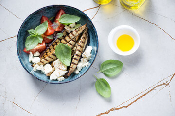 Salad with grilled eggplant and cheese served in a blue bowl, top view on a beige stone background, horizontal shot