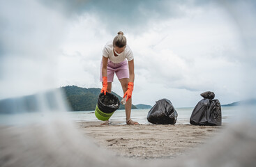 A female ecologist volunteer cleans the beach on the seashore from plastic and other waste