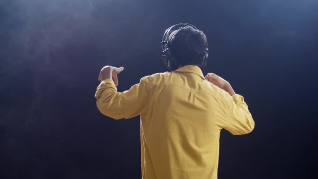 Back View Of A Young Boy With Headphone Rapping Into A Condenser Microphone On The White Smoke Black Background
