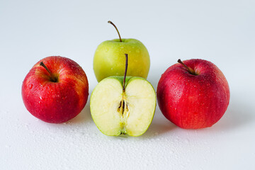 Red, yellow and green apples cut and whole on a white plain surface, four ripe fruits are covered with water drops isolated, lie neatly in front of the viewer, close-up of a still life