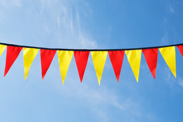 Festive ribbon of red and yellow triangle flags on the white clouds and blue sky background. Celebration party, holiday fair, festival decorations.