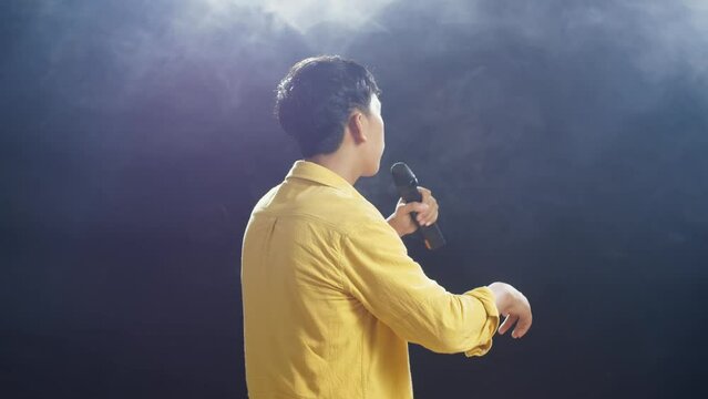 Back View Of A Young Boy Holding A Microphone And Rapping On The White Smoke Black Background
