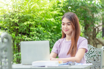 beauty woman doing freelance work in garden. Asian woman using laptop at home back yard with tree background copy space.