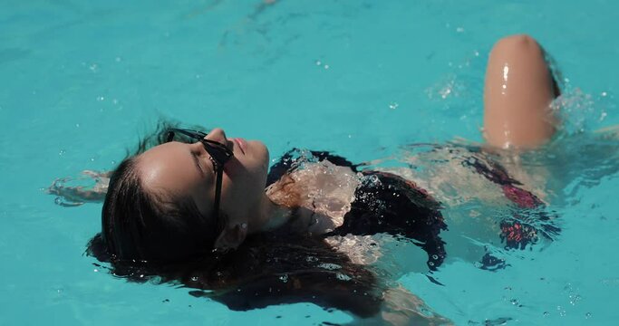 Beautiful woman swimming in the pool, slow motion, relaxing and resting in a water