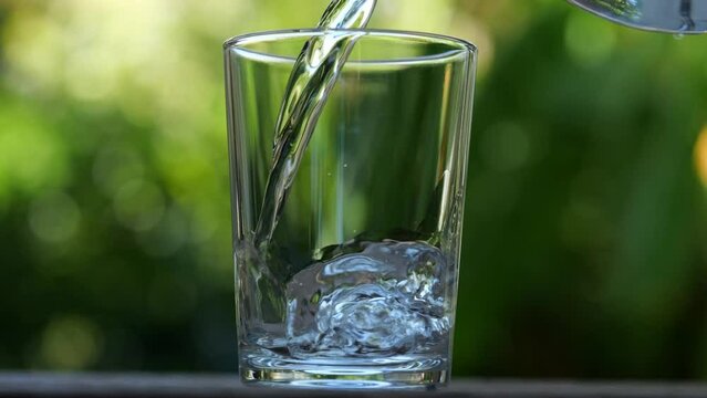 Pouring water into transparent glass in slow motion at outdoor. Concept pour water. Select focus 4K resolution.