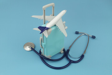 Airplane on suitcase and stethoscope on blue background. Travel insurance, medical tourism, health care concept. - obrazy, fototapety, plakaty