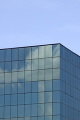 Clouds reflect in the windows of a generic modern office building's facade with clear blue sky in the background