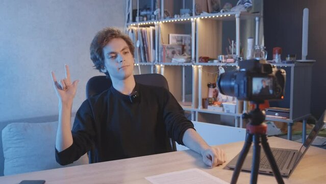 The blogger shows Rock sign from his fingers to the turned on camera. dark-haired guy. Vlogger, streamer. Young man. Handsome guy. 