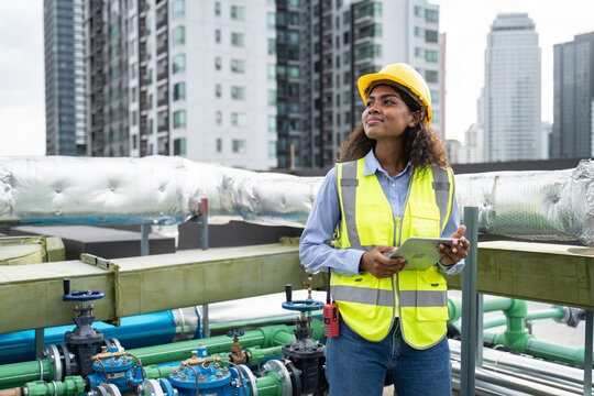 Service Engineer Woman Dark Skin Wearing Uniform And Safety Helmet Under Inspection And Checking Production Process,HVAC System (Heating,Ventilation And Air Conditioning) On Factory Station By Tablet.