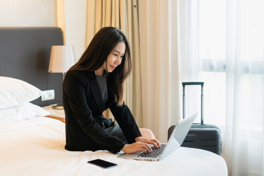 Smiling businesswoman working on laptop computer in bed at hotel. Business trip, people and technology concept, copy space