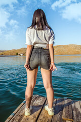 Young girl in shorts on the pier on the river, rear view