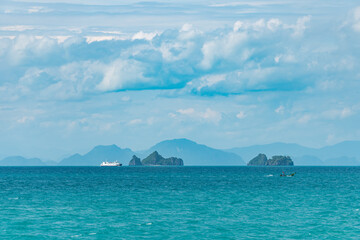 View of the turquoise sea and islands on a sunny summer day.  A ship sails in the distance.  Mountain silhouettes in the background.