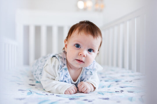 Happy Aussie baby smiling at tummy time in cot in bedroom