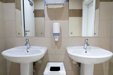 Pair of symmetrical sinks in a modern public toilet with paper towels and soap dishes