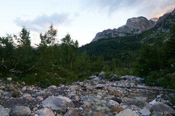 mountain river stream in alpine mountain and meadows at sunset in the evening