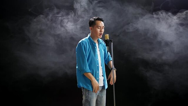 Side View Of Asian Man Rapping Into A Condenser Microphone On The Black Background
