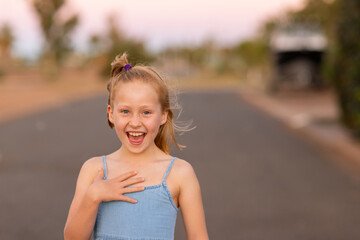 coquettish little blonde girl outside with wind in hair and smile on face