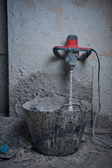 An industrial hand held cement mixing whisk in a dirty textured cement and concrete setting....