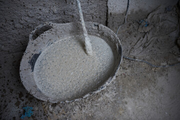 An industrial hand held cement mixing whisk in a dirty textured cement and concrete setting....