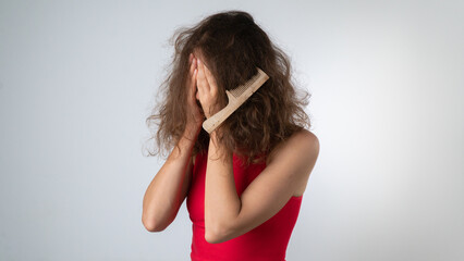 Upset woman with a tangled comb in her hair, problematic, naughty hair with split ends - obrazy, fototapety, plakaty