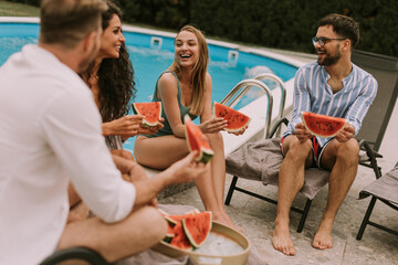 Young people sitting by the swimming pool and eating watermelon in the house backyard