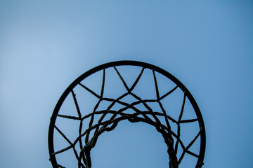 Silhouette of basketball hoop and net against blue sky