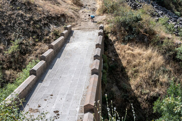 a stone bridge to nowhere and a tourist is looking at something on the edge of the bridge