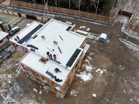 Roofing construction worker installing a flat roof. Bright blue sky in the background.