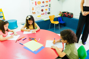 Diverse preschoolers coloring in their desks in kindergarten
