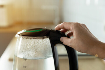 Close-up of a woman pressing the power switch on an electric kettle.Kettle for boiling water and...