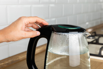 Close-up of a woman pressing the power switch on an electric kettle.Kettle for boiling water and making tea.Home appliances for making hot drinks.Space for copy.Place for text.