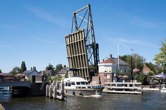 KOUDEKERK, NETHERLANDS - AUGUST 13 2022: Boat sails on the 'Oude Rijn' (Old Rhine) river under the opened steel drawbridge in the village of Koudekerk aan den Rijn, Netherlands