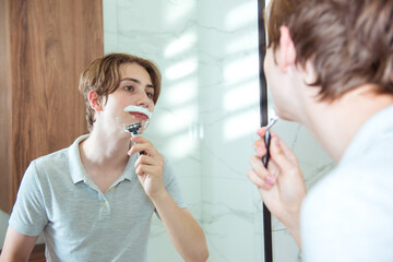 Young caucasian teen boy shaving beard in bathroom