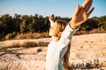 Lifestyle, happiness and people concept - child girl raising hands over nature landscape background