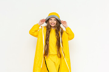 The child is covered by the hood of a raincoat from the rain on a white isolated background. A little girl with long hair and a big smile in a yellow raincoat.