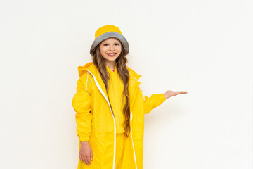 A little girl in a raincoat holds your advertisement in the palm of her hand and smiles broadly. A child in a yellow raincoat and panama hat on a white isolated background.