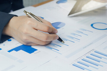 Close-up hand holding pen business woman  analyzing chart and graph showing changes on the market.