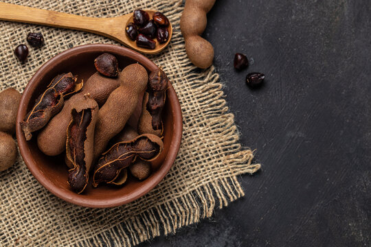 Tropical fruits, Tamarindo beans in shell on a brown butchers block on a dark background, healthy fruit. banner, menu, recipe place for text, top view