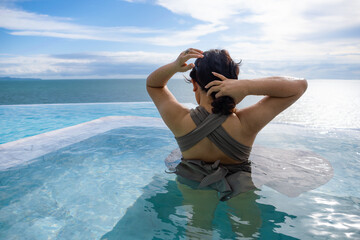 Female tourist playing in a swimming pool overlooking the sea.