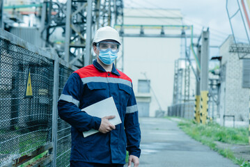 A masked power engineer during a pandemic inspects the modern equipment of an electrical substation...