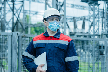 A masked power engineer during a pandemic inspects the modern equipment of an electrical substation...