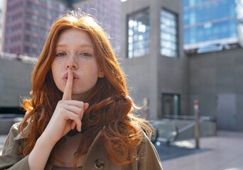 Hipster teen stylish cool redhead fashion girl model showing shh sign asking to keep secret, be...