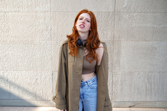 Cool stylish redhead fashion hipster girl generation z model standing on urban wall background looking bored, annoyed or displeased.